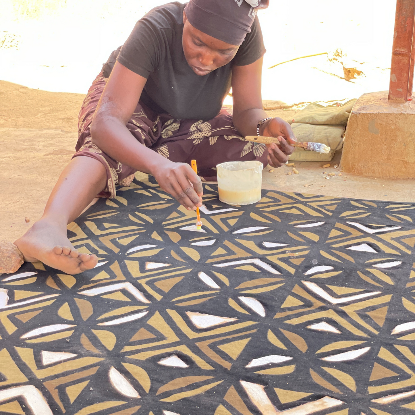 une femme entrain du mettre du savon sur une étoffe avec des motifs en bogolan