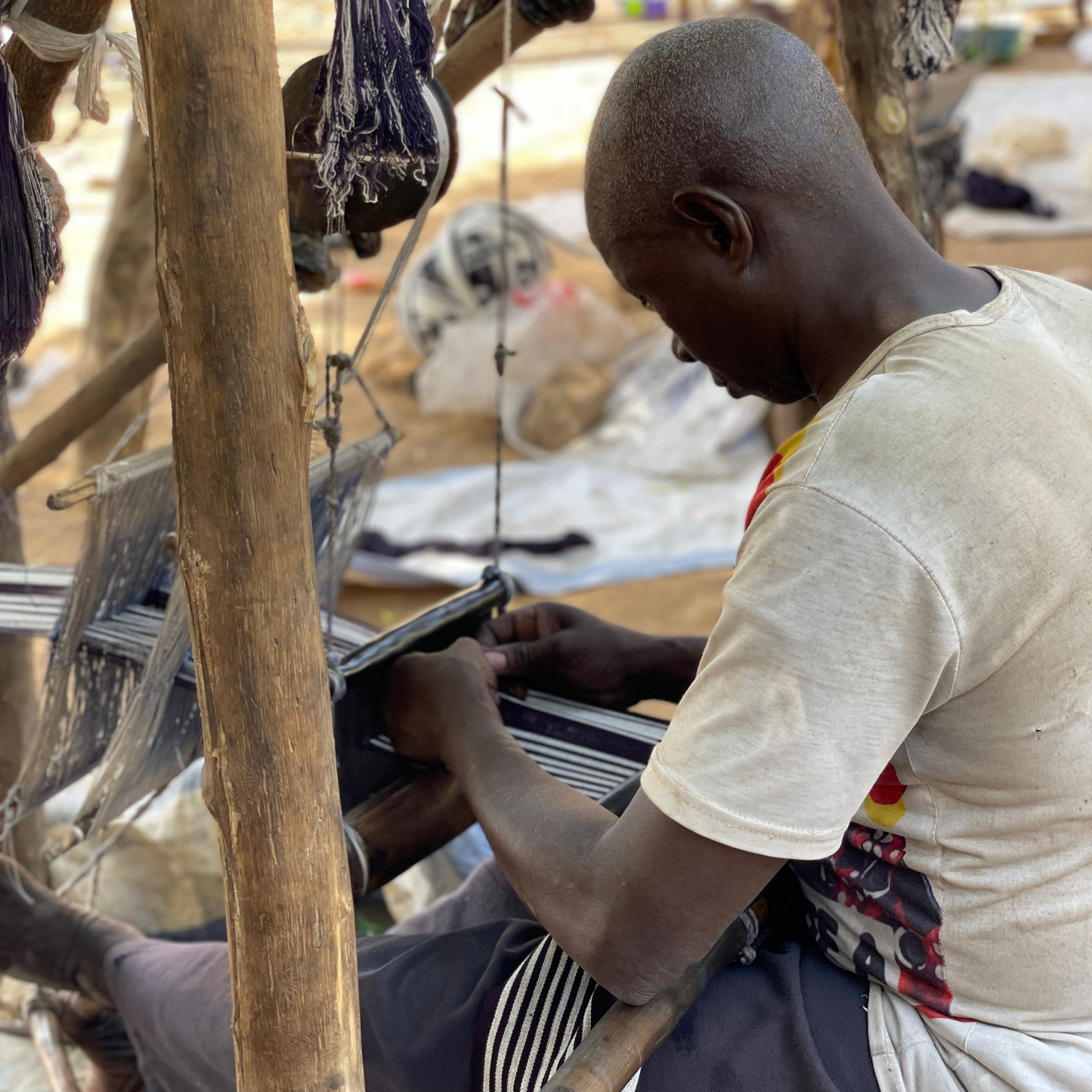 Un homme entrain de tisser une étoffe à l'aide de son métier à tisser artisanal