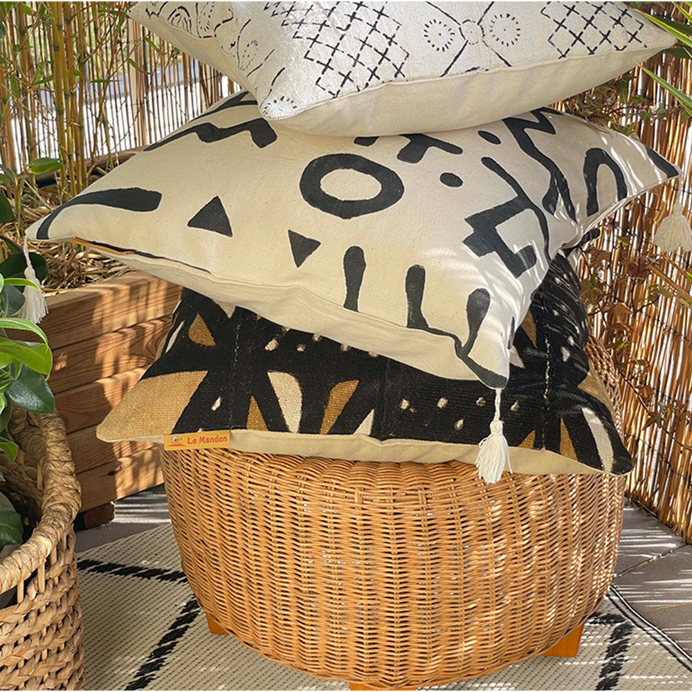 Coussin en bogolan empilés l'un sur l'autre sur un pouf en osier - Bogolan cushion stacked one on top of the other on a wicker pouf