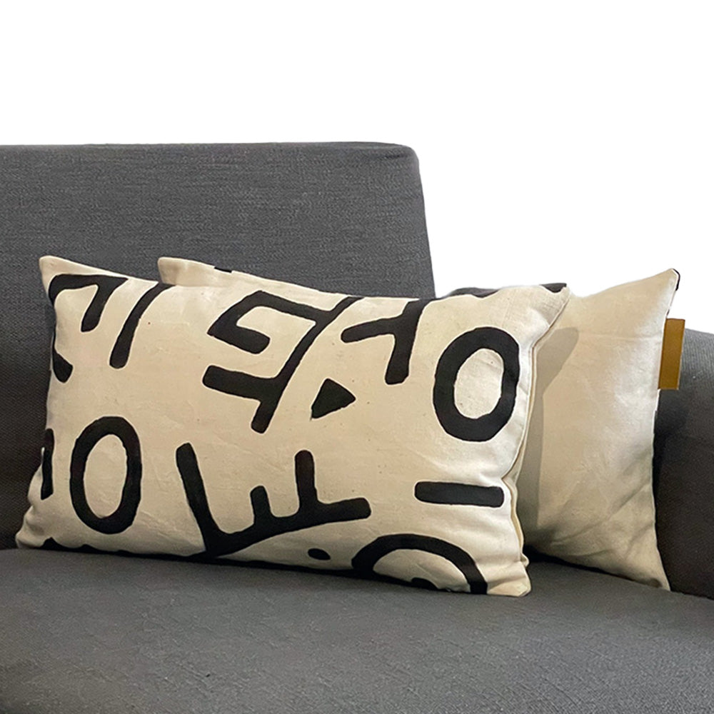 Coussin blanc ecru de forme rectangulaire avec des motifs noirs bogolan sur canapé gris - Rectangular ecru white cushion with black bogolan patterns on gray sofa