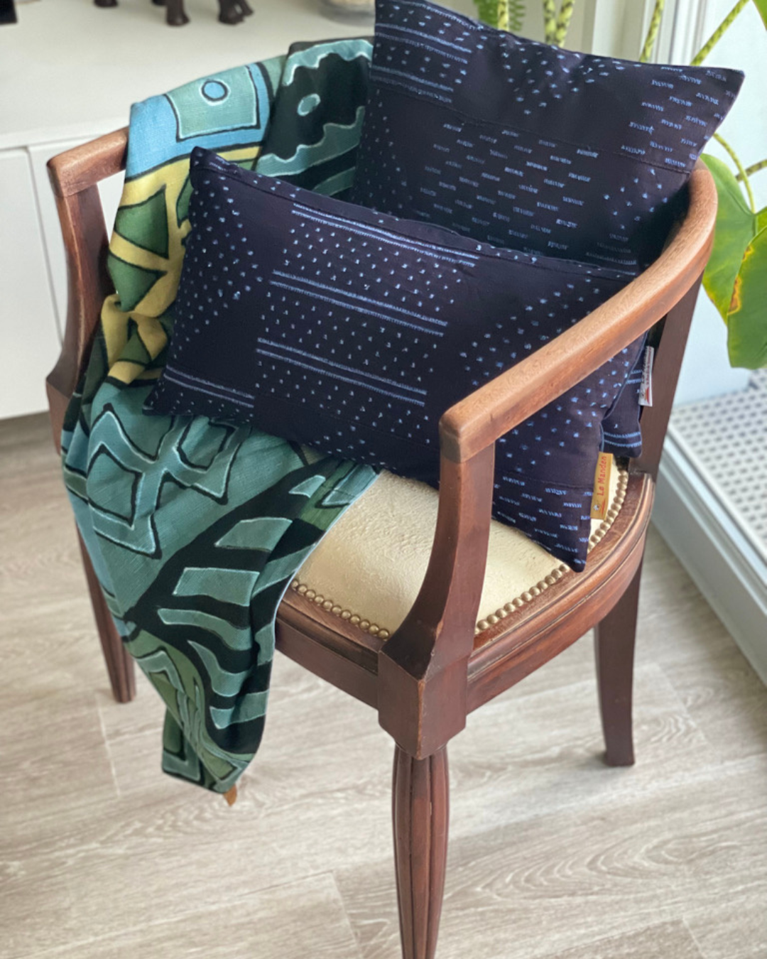 Coussin de forme carrée et rectangle de couleur bleu indigo avec des motifs bleu clair sur une chaise accompagné d'un plaid bleu - Square and rectangle cushion in indigo blue with light blue patterns on a chair accompanied by a blue throw
