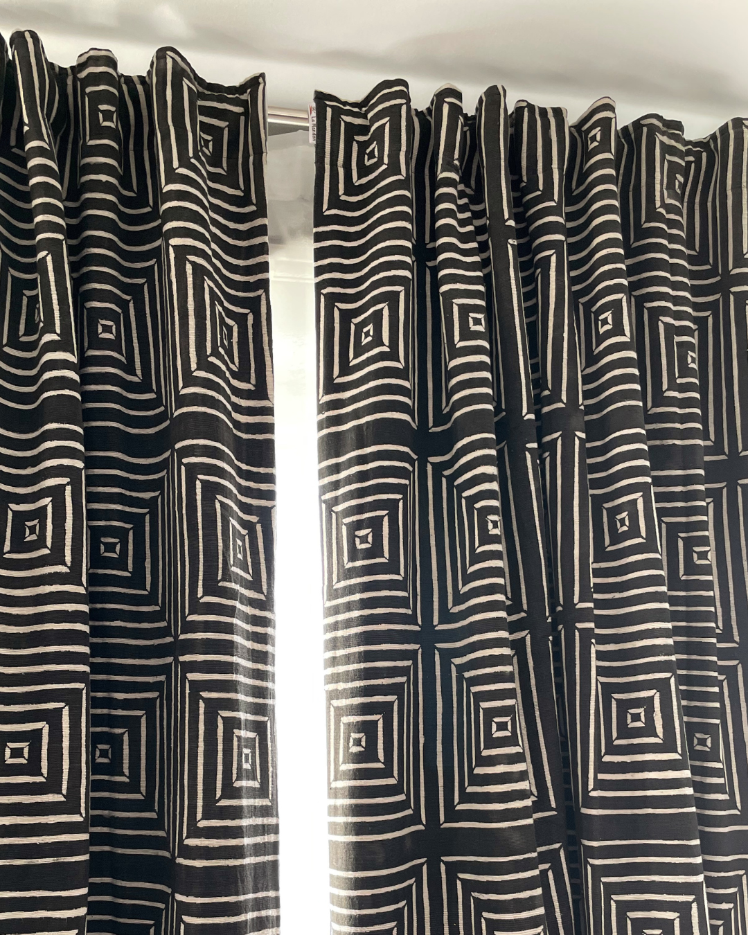 Rideau de couleur noir en bogolan de forme géométique blanche fixé à une fenêtre - Black bogolan curtain in white geometric shape attached to a window