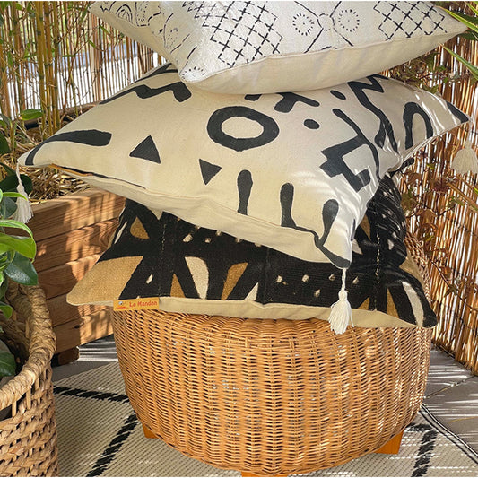 Coussin en bogolan empilés l'un sur l'autre sur un pouf en osier - Bogolan cushion stacked one on top of the other on a wicker pouf