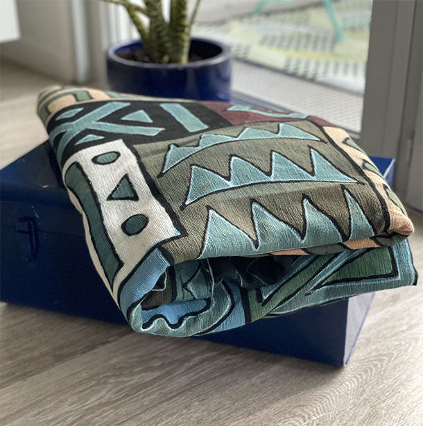 Plaid de couleur bleu avec des formes géométriques de couleurs blanche noir marron blanche et verte sur une malle-Blue plaid with geometric shapes in white, black, brown, white and green colors on a trunk