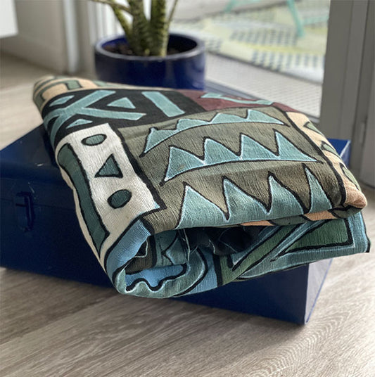 Plaid de couleur bleu avec des formes géométriques de couleurs blanche noir marron blanche et verte sur une malle-Blue plaid with geometric shapes in white, black, brown, white and green colors on a trunk